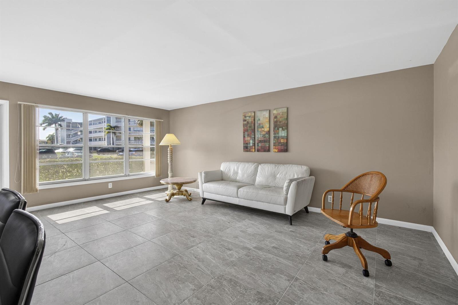 A living room with gray tile floors, a white sofa, and a wooden rolling chair — 105 Greenbrier C, West Palm Beach FL 33417, WEST PALM BEACH, FL