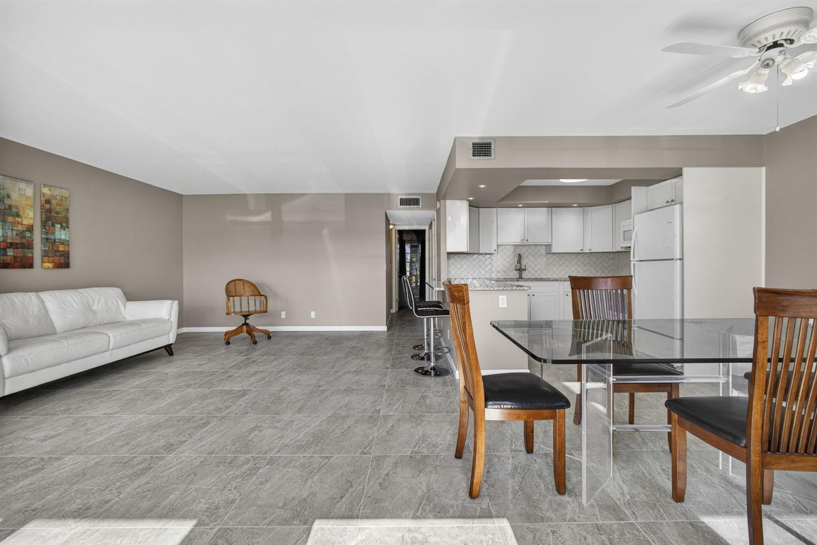 A living and dining area features gray tile flooring, a white sofa, and a kitchen — 105 Greenbrier C, West Palm Beach FL 33417, WEST PALM BEACH, FL