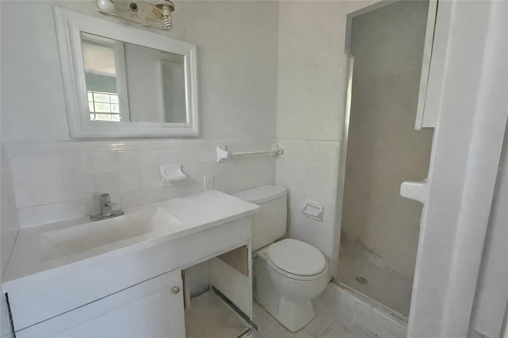 A bathroom features a white vanity, a toilet, and a tiled walk-in shower — 23 NE 6TH STREET, CHIEFLAND, FL