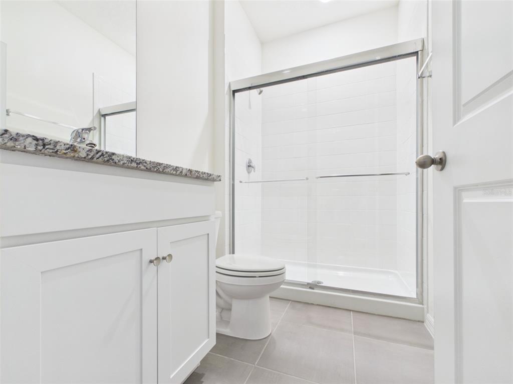A bathroom features a white vanity with granite countertop, a toilet, and a glass-enclosed shower — 5962 SW 80TH LN, OCALA, FL