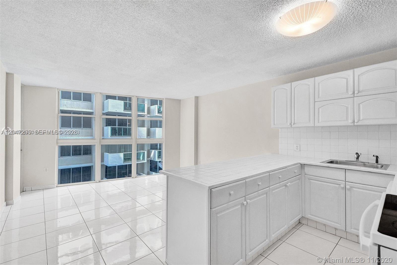 A kitchen with white cabinets and tiled countertops opens into a bright living area — 1228 West Ave # 613, Miami Beach FL 33139, MIAMI BEACH, FL
