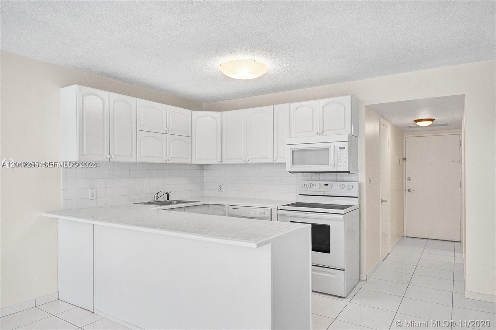A white kitchen features a breakfast bar, white cabinetry, and white appliances — 1228 West Ave # 613, Miami Beach FL 33139, MIAMI BEACH, FL