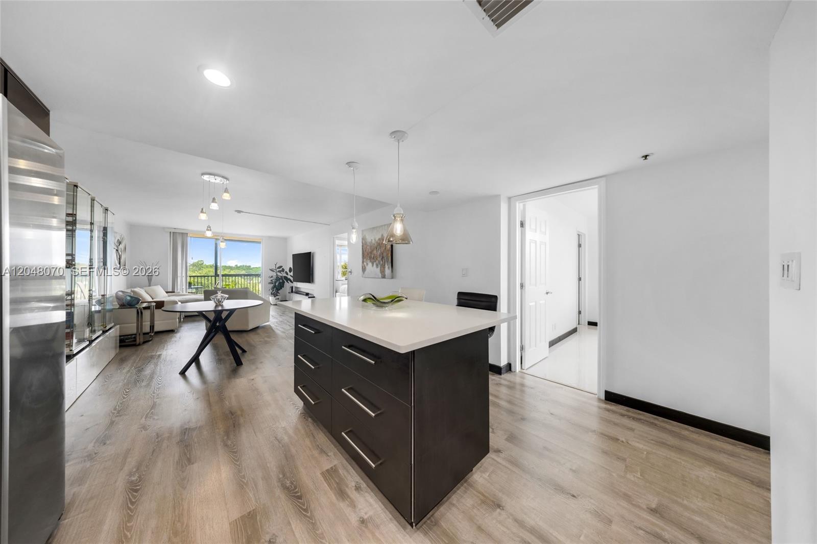 A modern kitchen island with dark cabinets and a white countertop sits in an open-concept room — 3001 W Rolling Hills Cir # 610, Davie FL 33328, DAVIE, FL