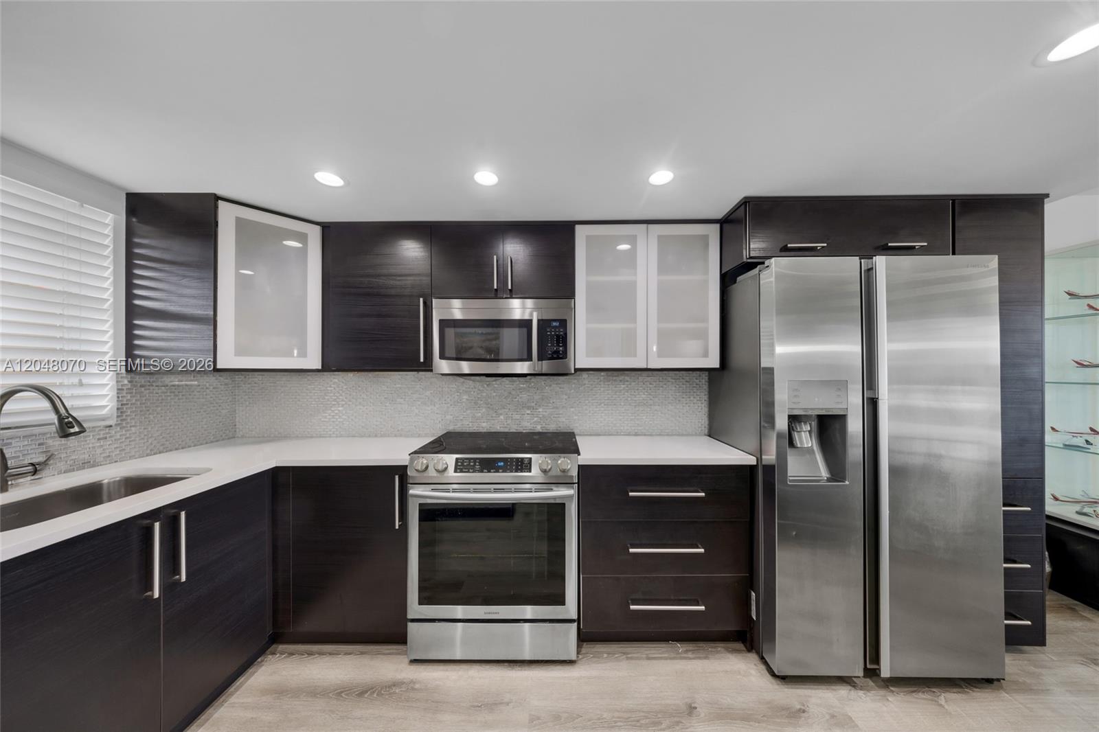 A modern kitchen features dark wood cabinetry, stainless steel appliances, and white countertops — 3001 W Rolling Hills Cir # 610, Davie FL 33328, DAVIE, FL