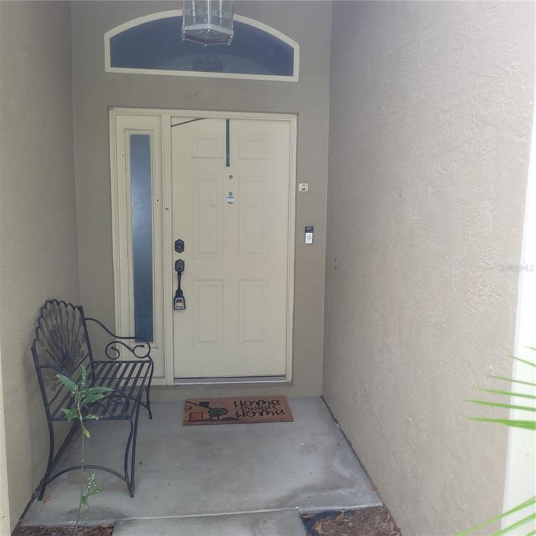 A front entryway features a light-colored door with a sidelight, a bench, and a doormat — 10831 PEPPERSONG DRIVE, RIVERVIEW, FL