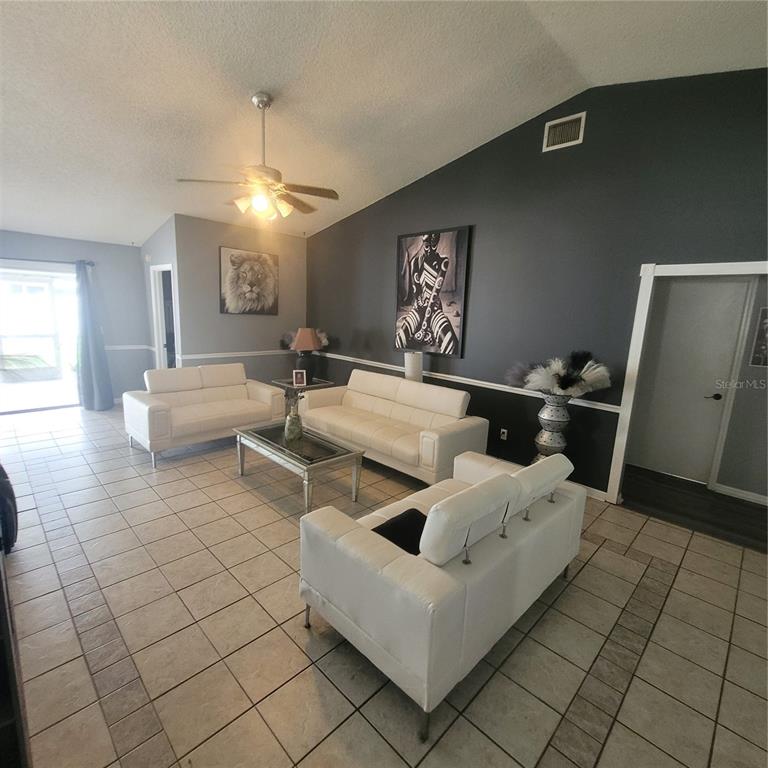 A living room features white leather sofas, a glass coffee table, and dark accent walls — 10831 PEPPERSONG DRIVE, RIVERVIEW, FL