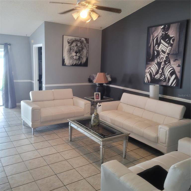 A living room features white leather sofas, a glass coffee table, and large wall art — 10831 PEPPERSONG DRIVE, RIVERVIEW, FL