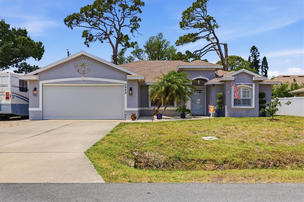 A single-story house with a two-car garage, a palm tree, and a compass wall ornament — 5948 ORCHIS ROAD, VENICE, FL