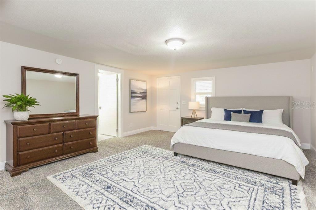A bedroom features a large bed, a wooden dresser with a mirror, and carpeted flooring — 4571 PARK STREET, JACKSONVILLE, FL