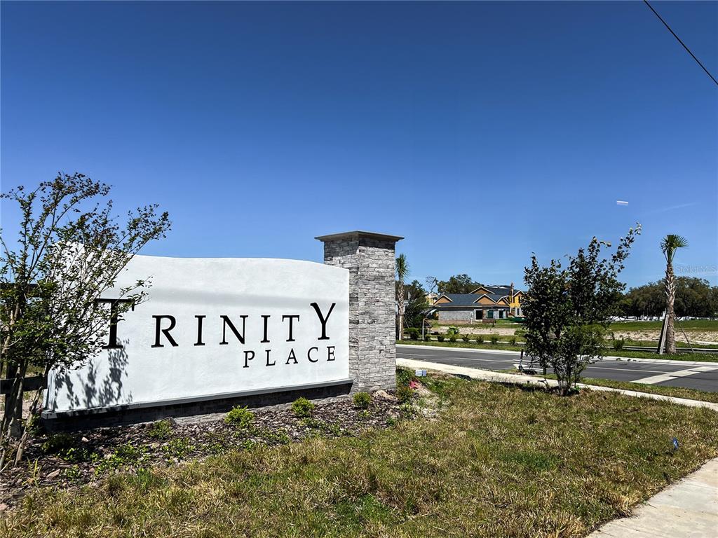 A stone and stucco monument sign for Trinity Place stands beside a road with new construction — 2060 IORIO STREET, ST CLOUD, FL