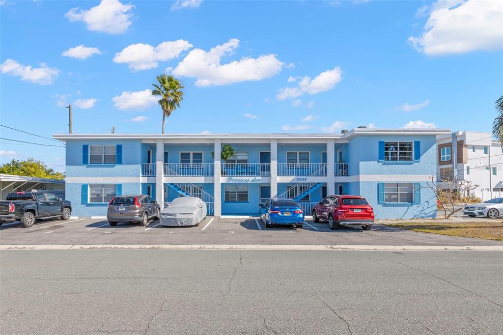 A two-story blue apartment building with a parking lot in front under a blue sky — 11025 2ND STREET E UNIT 8, TREASURE ISLAND, FL