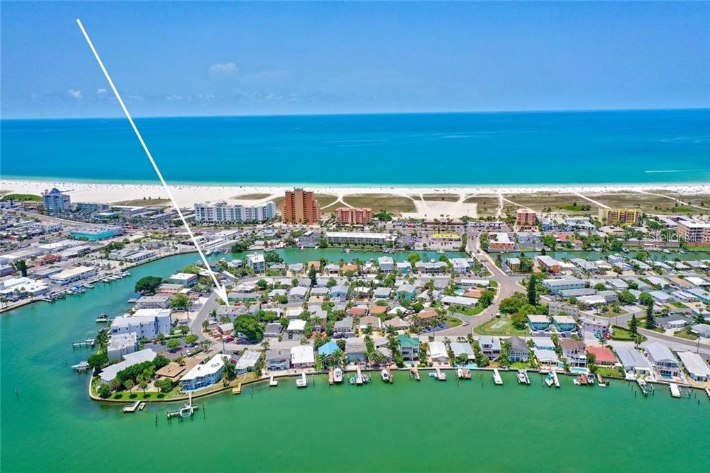 An aerial view shows a coastal neighborhood with houses, boat docks, and a nearby beach — 11025 2ND STREET E UNIT 8, TREASURE ISLAND, FL