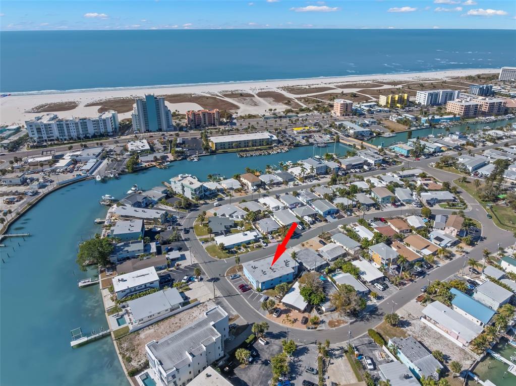 An aerial view shows a coastal neighborhood with a red arrow pointing to a building — 11025 2ND STREET E UNIT 8, TREASURE ISLAND, FL
