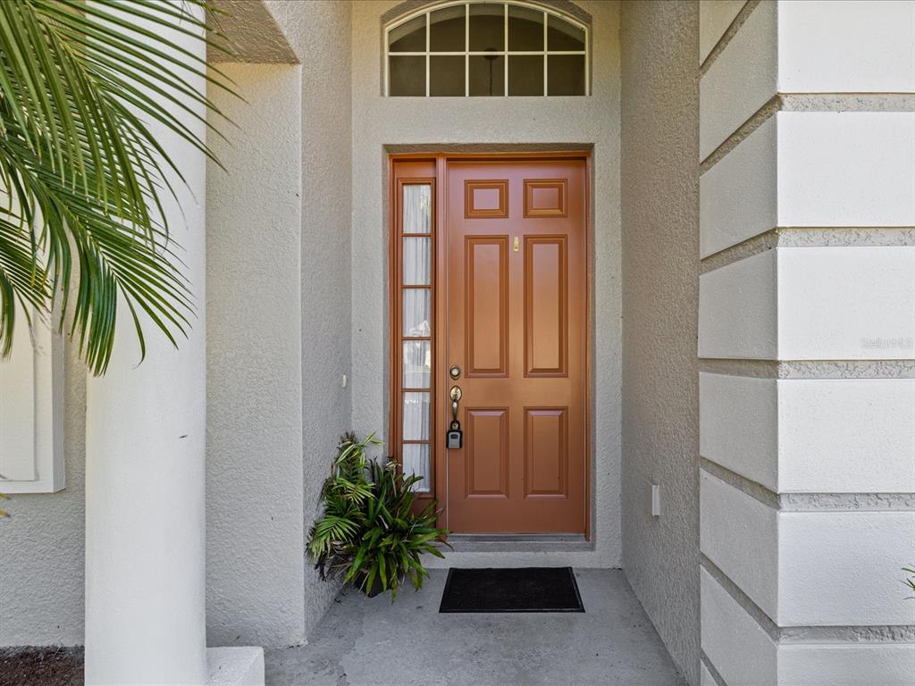 A brown front door with a side window and arched transom sits under a porch — 11448 MERGANSER WAY, NEW PORT RICHEY, FL