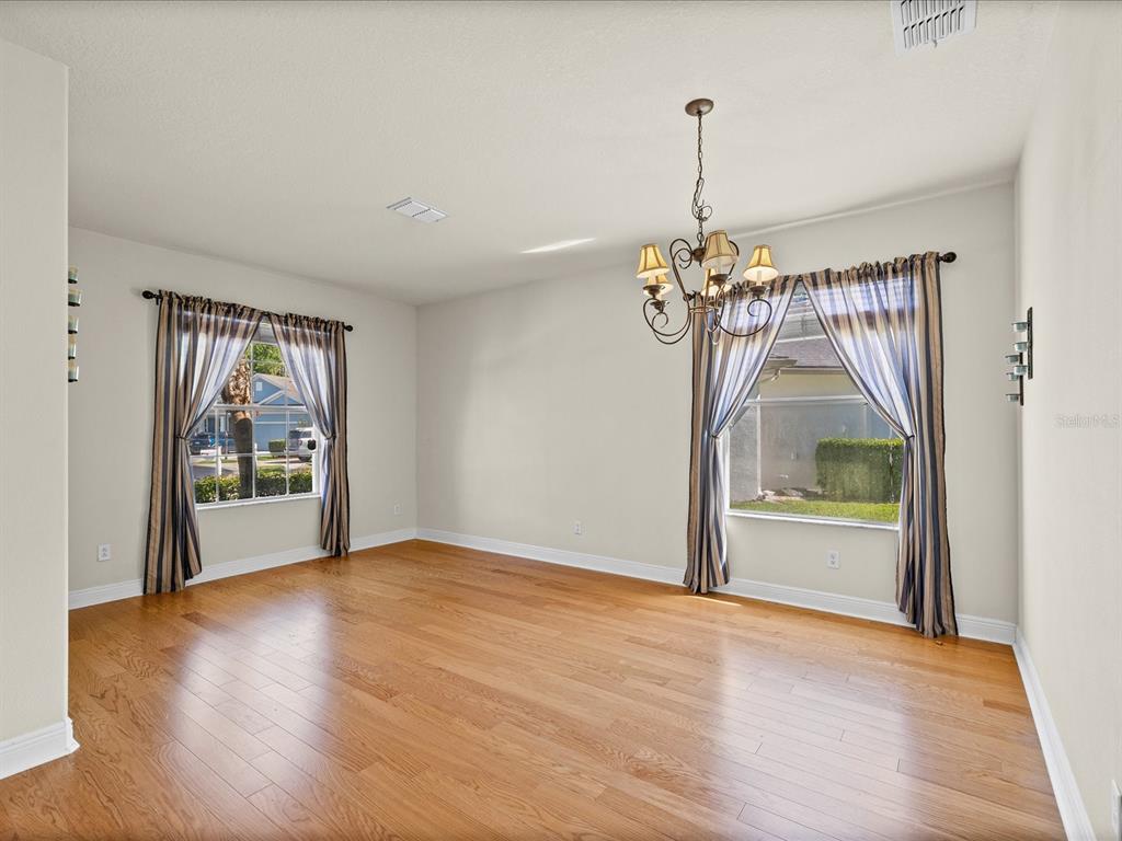 An empty dining room features hardwood floors, a chandelier, and two windows with striped curtains — 11448 MERGANSER WAY, NEW PORT RICHEY, FL