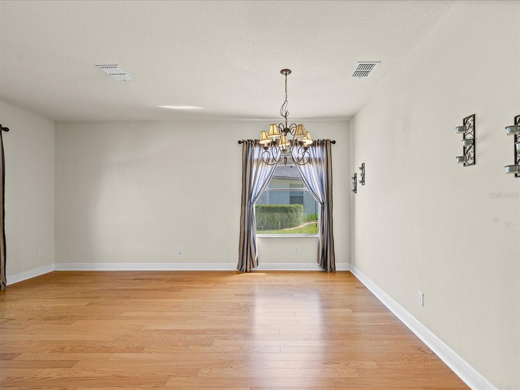 An empty dining room features hardwood floors, a chandelier, and a window with curtains — 11448 MERGANSER WAY, NEW PORT RICHEY, FL