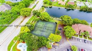 An aerial view shows two tennis courts surrounded by trees, a pond, and parking areas — 9938 Nob Hill Pl # 1838, Sunrise FL 33351, SUNRISE, FL