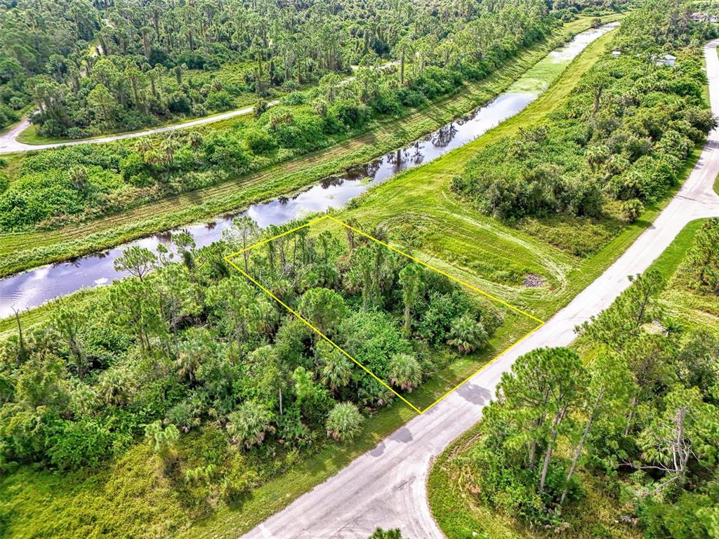 An aerial view shows a rectangular, wooded vacant lot bordered by a road and canal — BARCELONA DRIVE, NORTH PORT, FL