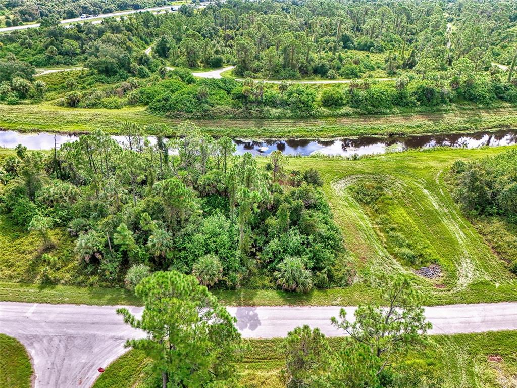 An aerial view shows a wooded lot, a canal, and a paved road — BARCELONA DRIVE, NORTH PORT, FL