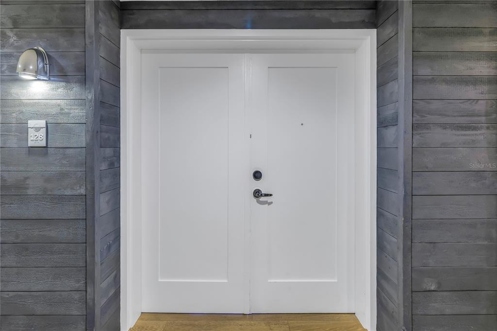 A white double door with a silver handle is set against gray horizontal wood siding — 5325 MARINA DRIVE UNIT 128, BRADENTON BEACH, FL