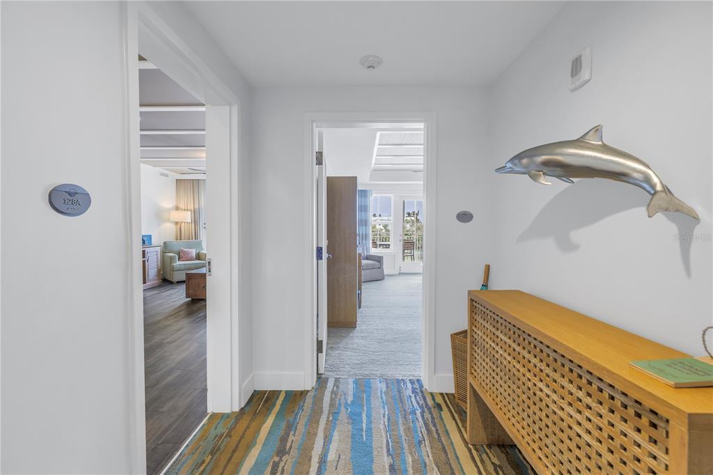 A hallway with a dolphin wall sculpture leads to two rooms with light-colored flooring — 5325 MARINA DRIVE UNIT 128, BRADENTON BEACH, FL