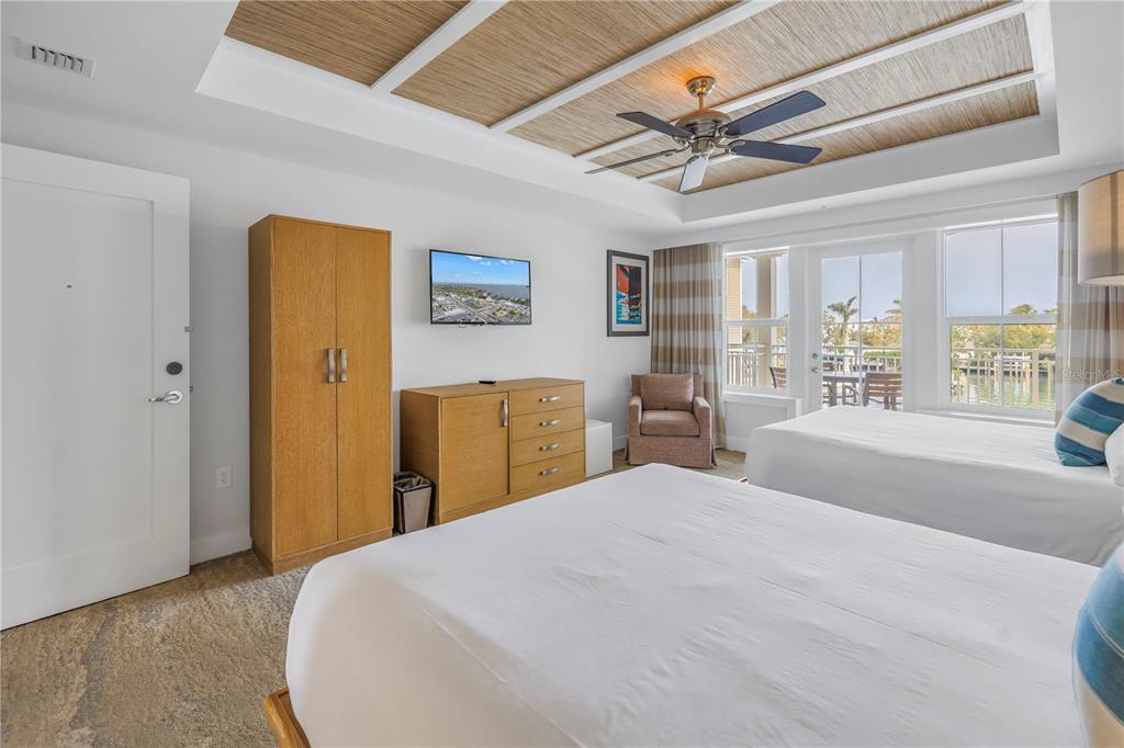 A bedroom features two beds, a wooden wardrobe, a dresser, and a tray ceiling — 5325 MARINA DRIVE UNIT 128, BRADENTON BEACH, FL