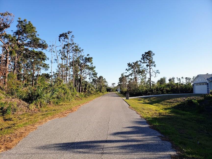 A paved road stretches through a wooded area with a house visible on the right — 4320 HOGRATH STREET, PORT CHARLOTTE, FL