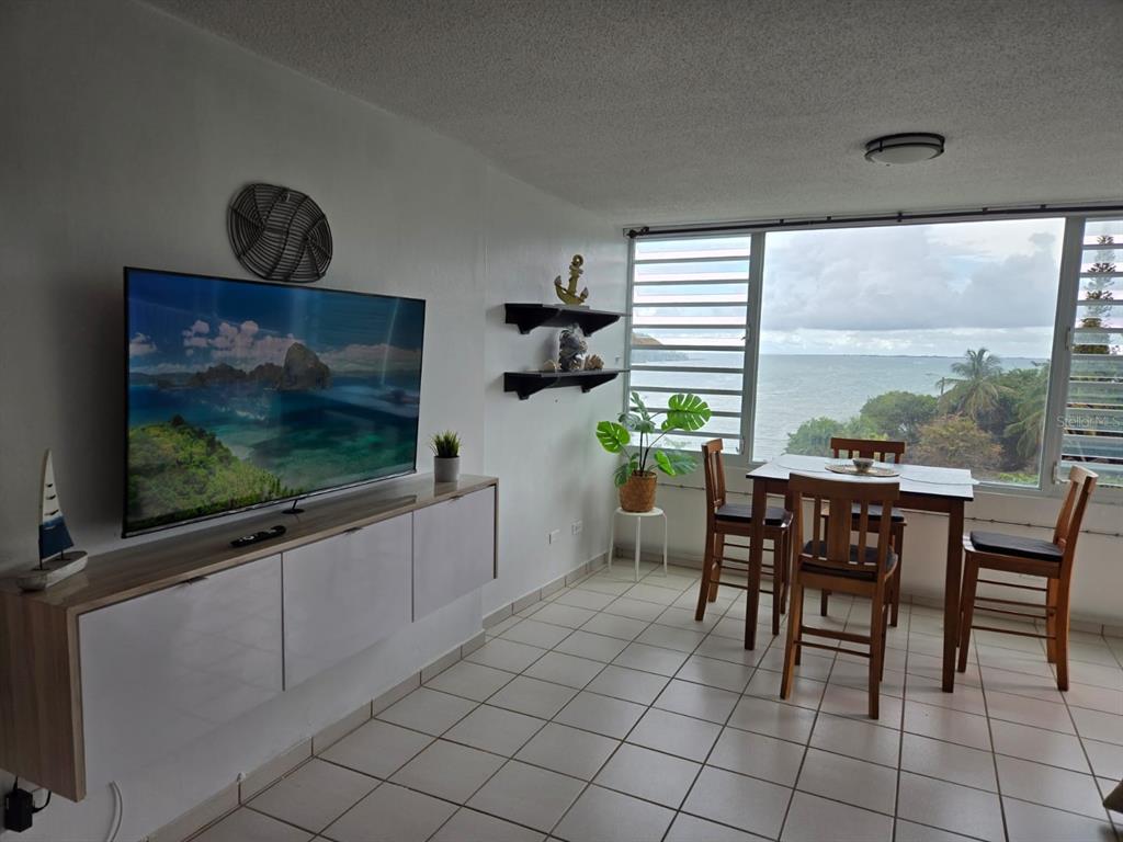 A living and dining area features white tile floors, a wall-mounted television, and ocean views — 100 AVENIDA MARINA VIEW DOS MARINAS CONDOMINIUM UNIT 303, FAJARDO, PR