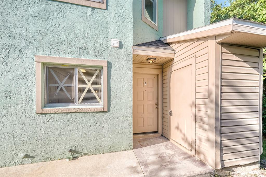 The exterior of a light green stucco building features a tan front door marked F — 283 GARDNER LANE UNIT F, KISSIMMEE, FL