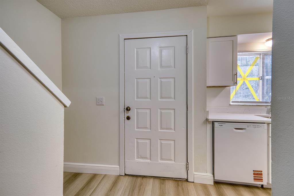 A white door stands next to a kitchen counter with a dishwasher and a window — 283 GARDNER LANE UNIT F, KISSIMMEE, FL