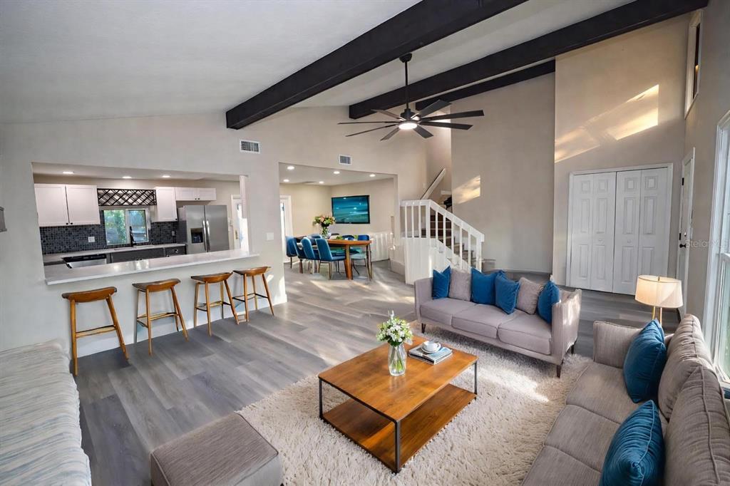 An open-concept living room, dining area, and kitchen with vaulted ceilings and exposed dark beams — 5667 CREEKWOOD DRIVE, SARASOTA, FL
