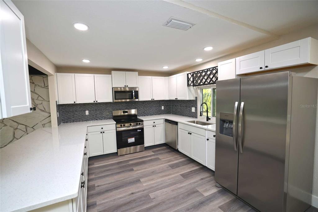 A kitchen features white cabinets, stainless steel appliances, quartz countertops, and dark mosaic tile backsplashes — 5667 CREEKWOOD DRIVE, SARASOTA, FL