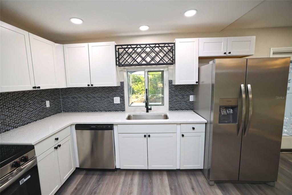 A kitchen features white cabinets, stainless steel appliances, a black tiled backsplash, and light countertops — 5667 CREEKWOOD DRIVE, SARASOTA, FL