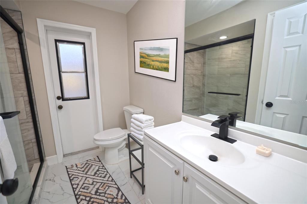 A bathroom features a white vanity, a toilet, a glass shower, and a patterned rug — 5667 CREEKWOOD DRIVE, SARASOTA, FL