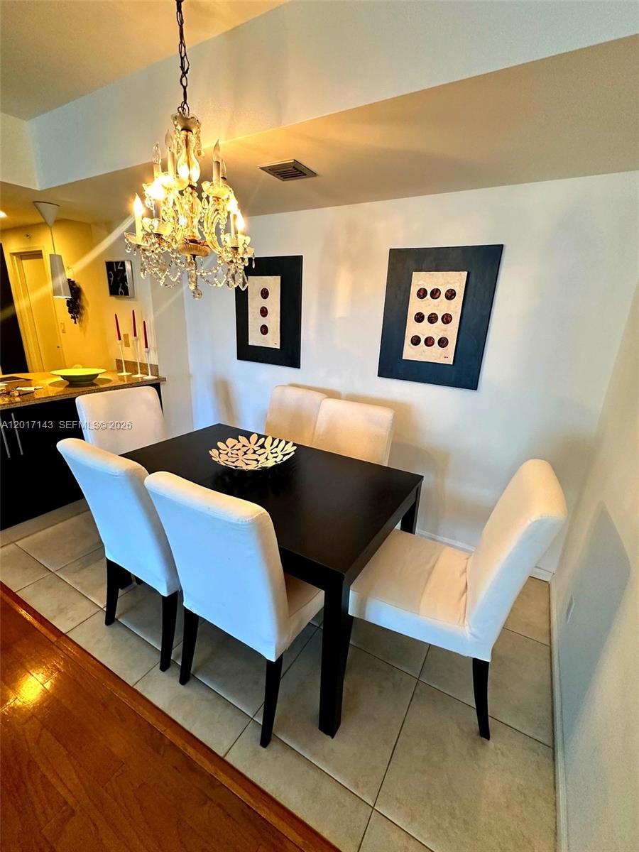 A dining area features a dark table, four white chairs, and a crystal chandelier — 1370 S Ocean Blvd # 902, Pompano Beach FL 33062, POMPANO BEACH, FL