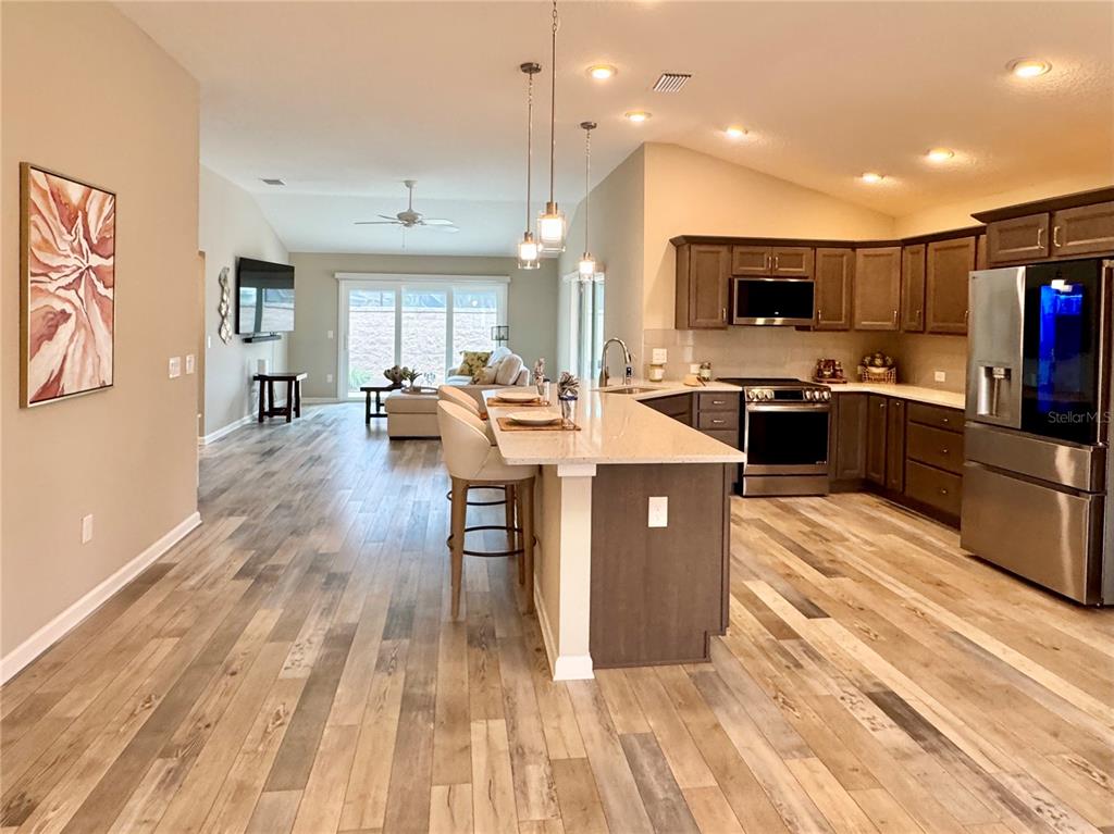 An open-concept kitchen with a granite island overlooks a living area with wood-look flooring — 3568 FARRELL AVENUE, THE VILLAGES, FL