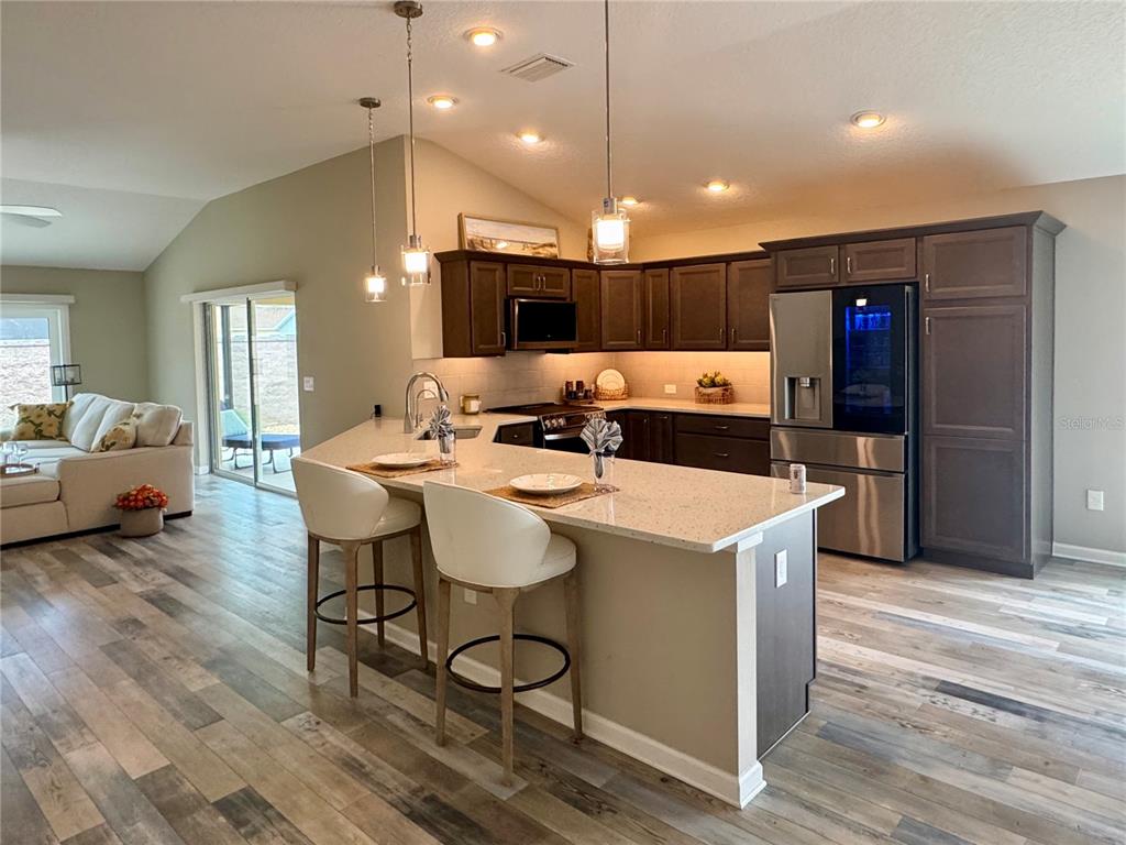A modern kitchen features dark wood cabinets, quartz countertops, and a breakfast bar with stools — 3568 FARRELL AVENUE, THE VILLAGES, FL