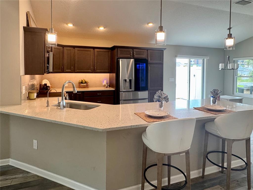 A kitchen features dark wood cabinets, light quartz countertops, a breakfast bar, and pendant lighting — 3568 FARRELL AVENUE, THE VILLAGES, FL