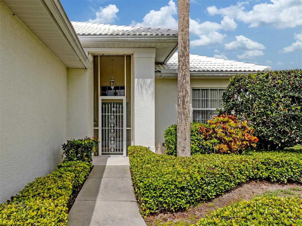 A concrete walkway leads to a white front door with a decorative security gate — 737 POND LILY WAY, VENICE, FL