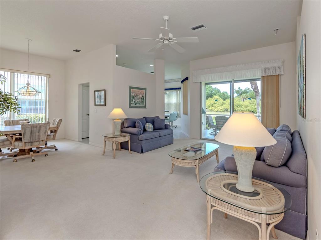 A living room with blue sofas, glass-topped tables, and a sliding door to a patio — 737 POND LILY WAY, VENICE, FL