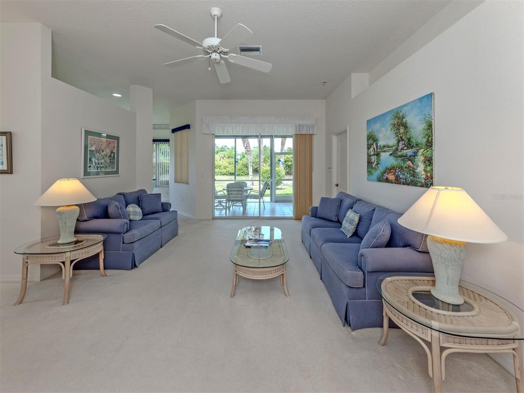 A living room features two blue sofas, glass-topped tables, and a sliding door to a patio — 737 POND LILY WAY, VENICE, FL