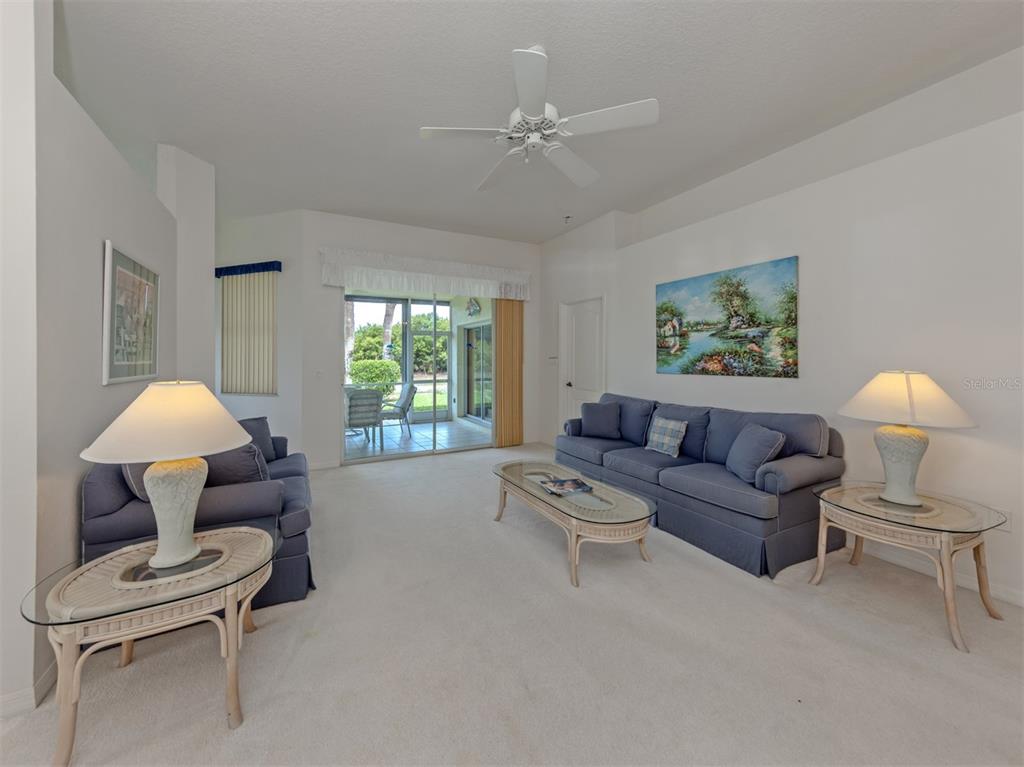 A living room features blue sofas, glass-topped rattan tables, a ceiling fan, and sliding glass doors — 737 POND LILY WAY, VENICE, FL