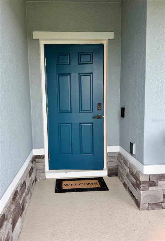 A blue front door with a keypad lock is framed by stone veneer and light-colored walls — 1562 LANDON LANE, HAINES CITY, FL