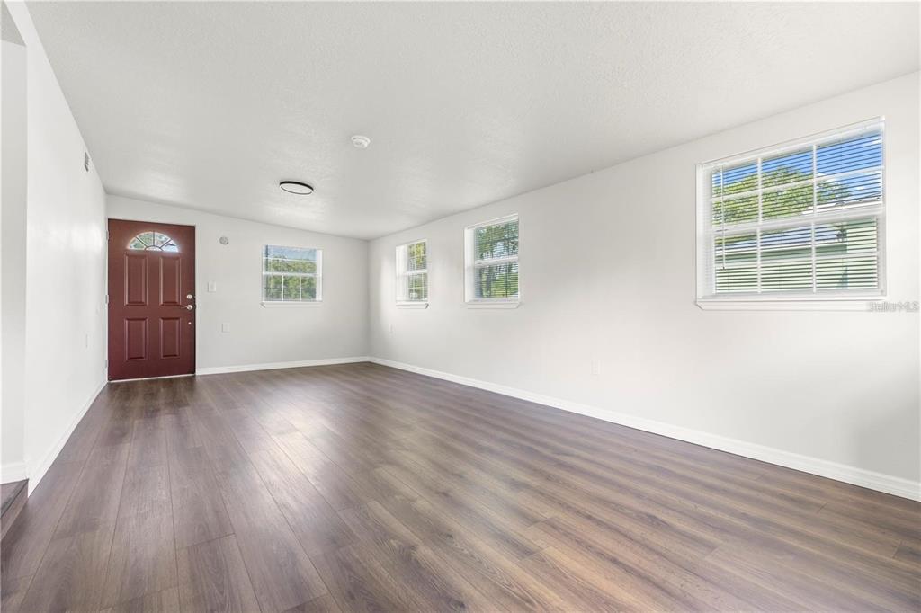 An empty living room features white walls, dark wood-look flooring, and several windows — 3013 LAUREL AVENUE, LAKE WALES, FL
