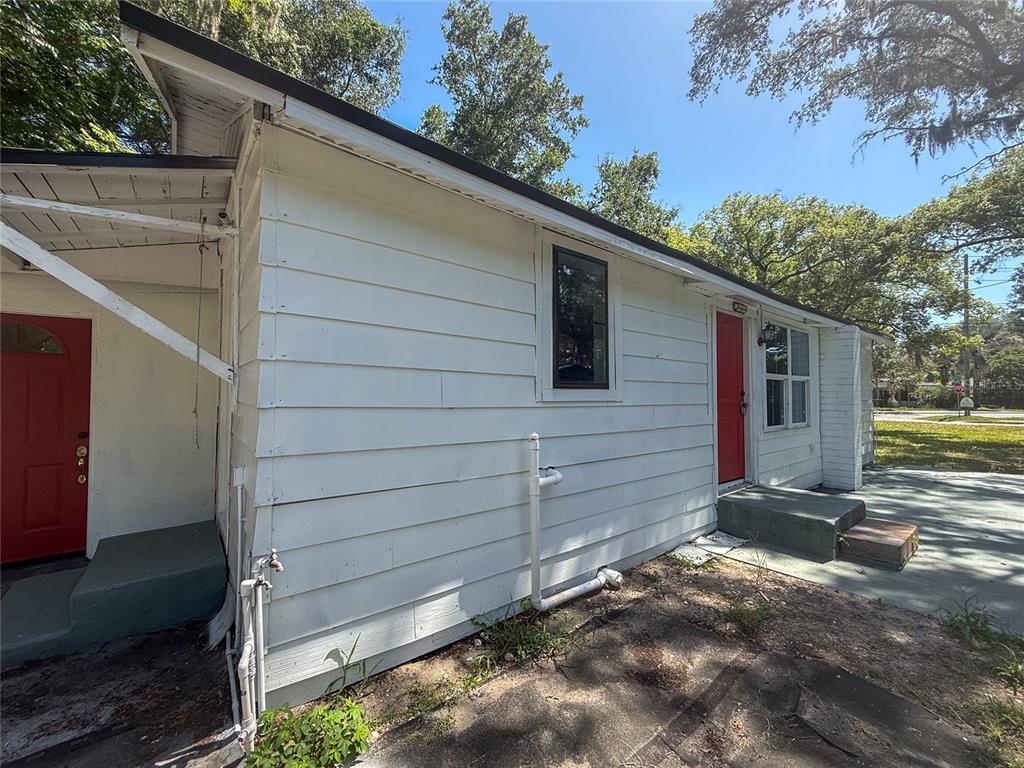 The exterior of a white-sided house features two red doors and exposed plumbing pipes — 1002 TILDEN AVENUE, APOPKA, FL