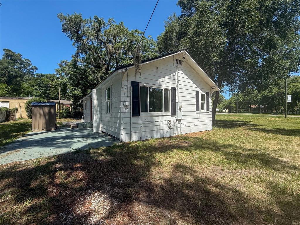 A white, single-story house with black shutters sits on a grassy lot with trees — 1002 TILDEN AVENUE, APOPKA, FL