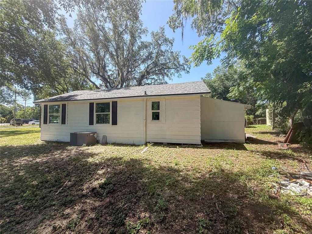 The exterior of a white, single-story house features a shingled roof and surrounding trees — 1002 TILDEN AVENUE, APOPKA, FL