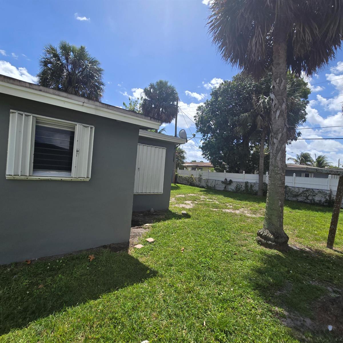 The exterior of a gray house features white hurricane shutters and a large palm tree — 3860 NW 8th Place, Lauderhill FL 33311, LAUDERHILL, FL