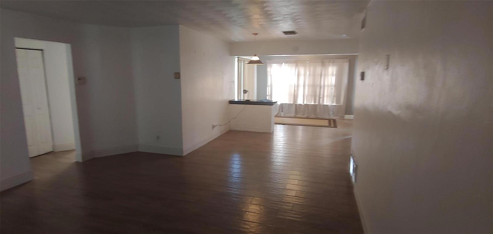An interior view of a living area with wood-look flooring and a kitchen pass-through window — 3860 NW 8th Place, Lauderhill FL 33311, LAUDERHILL, FL