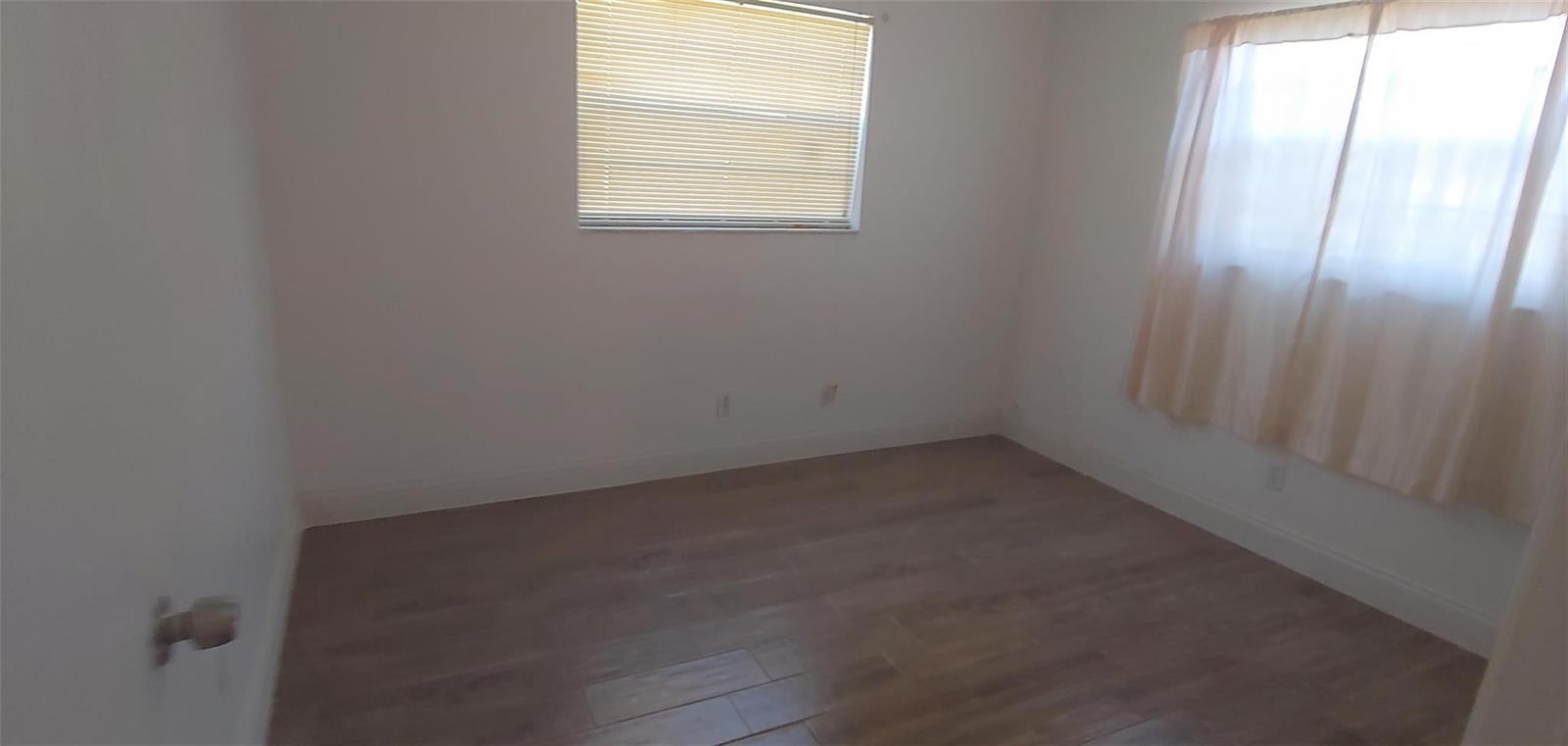 An empty bedroom features white walls, light wood-look flooring, and two windows with coverings — 3860 NW 8th Place, Lauderhill FL 33311, LAUDERHILL, FL